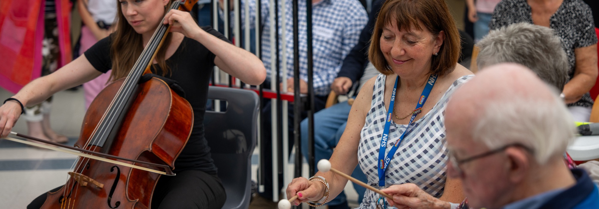 A STROKESTRA performance in North Point shopping centre in Hull, a woman with an NHS lanyward smiling and playing the xylophone with stroke patients, and an RPO cellist playing next to her