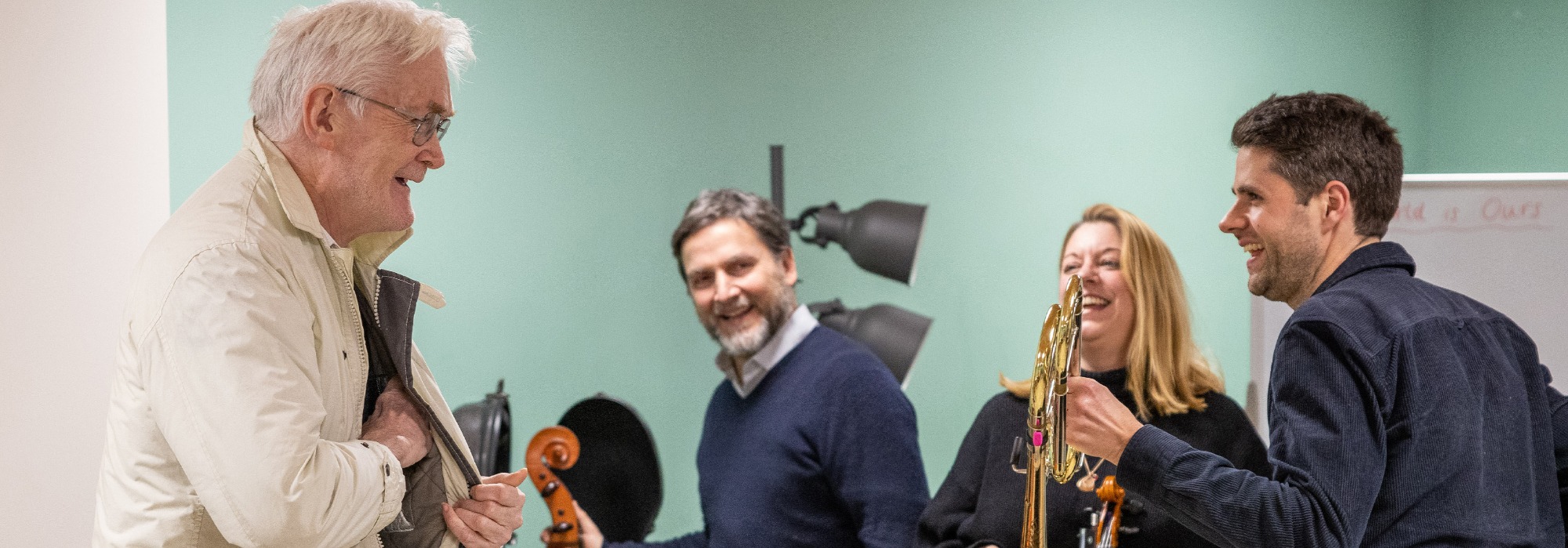 An RPO cellist, trombonist and violin laughing and smiling with an older man