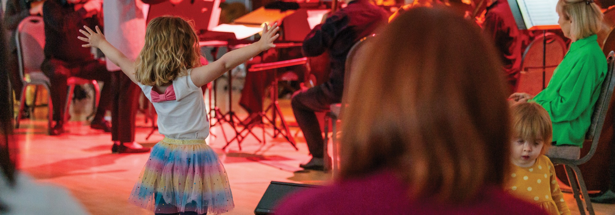 A young girl stanidng in front of the Orchestra at a Relaxed Performance and stretching her arms out