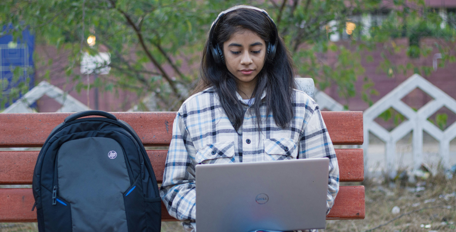 A student with a laptop sitting on a bench listening to music