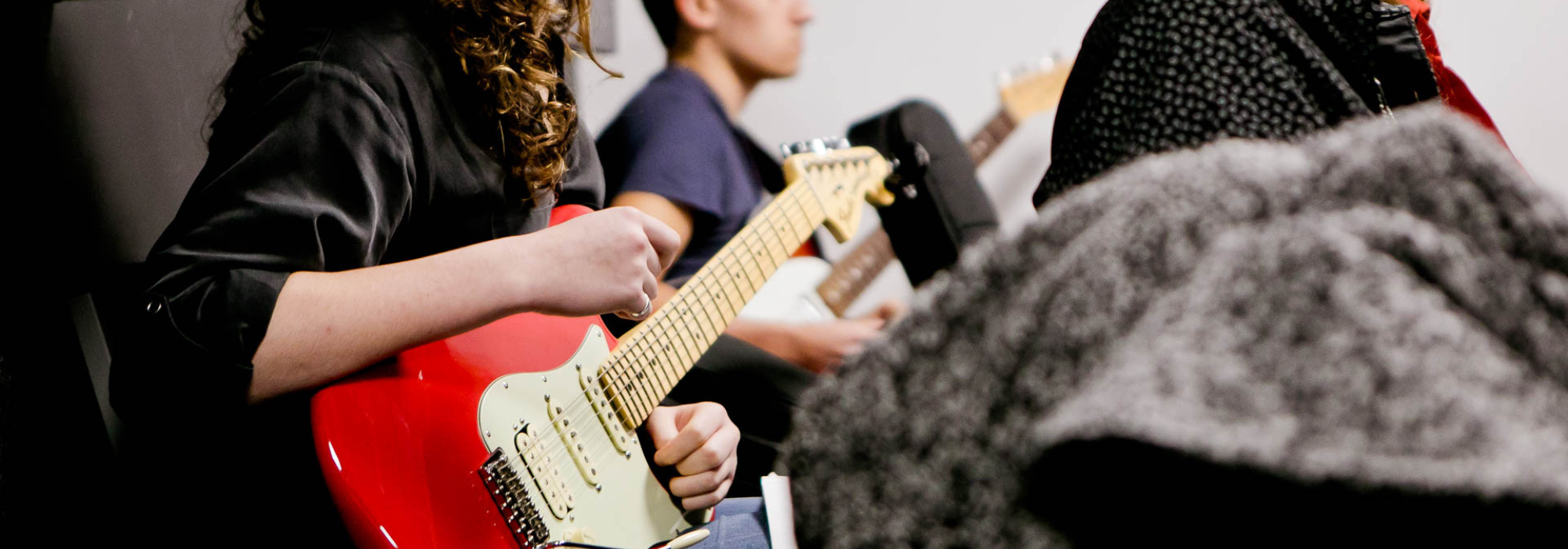 Hero banner of a female playing a red, electric guitar